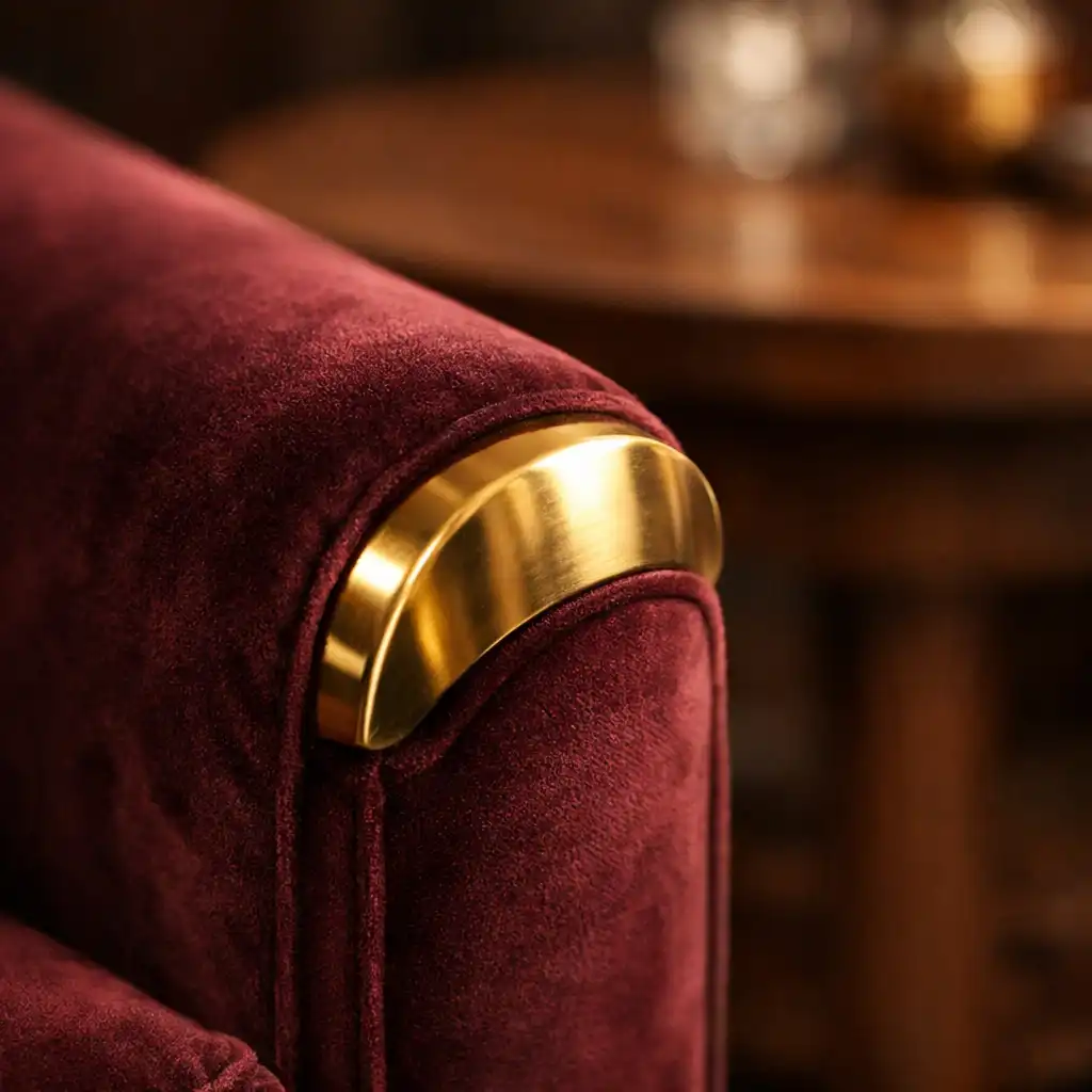 Gros plan sur un accoudoir de fauteuil en velours bordeaux avec finition en laiton et table en bois de noyer en arrière-plan